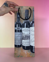 Hand holding a decorative wine gift bag with wine bottle designs on a gradient background