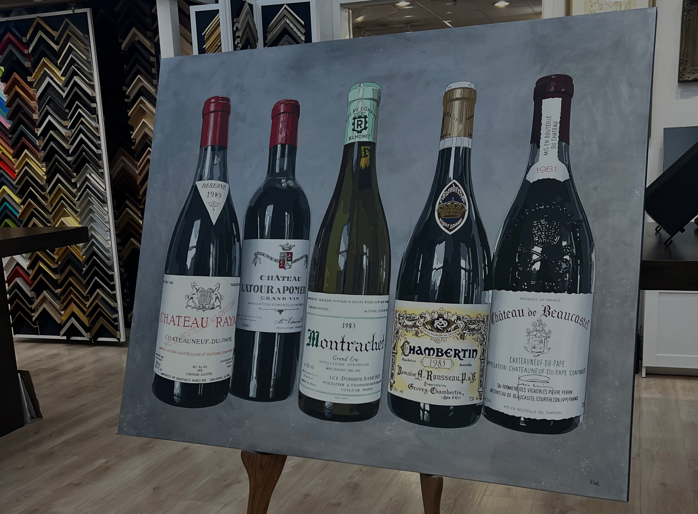 Painting of five wine bottles on an easel with a blurred indoor background