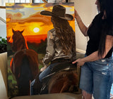 Person holding a painting of a cowboy and horse with a sunset background